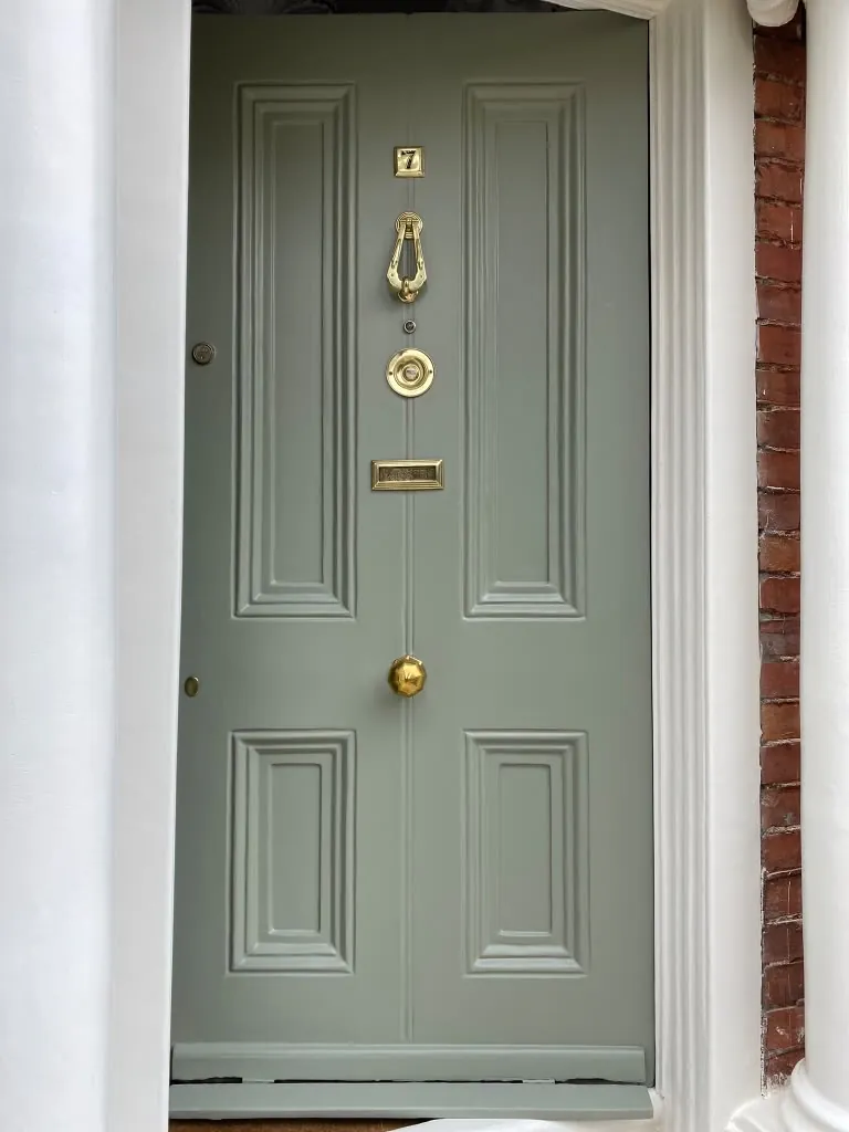 Front door painted soft grey-green with a brass knocker
