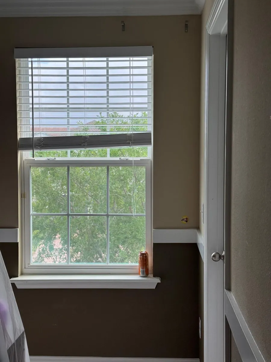 Bedroom window wall with tan paint over a brown band and a white chair rail before painting