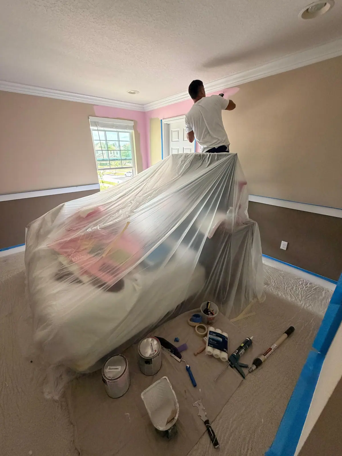 Bedroom furniture wrapped in plastic and the floor taped, walls in progress